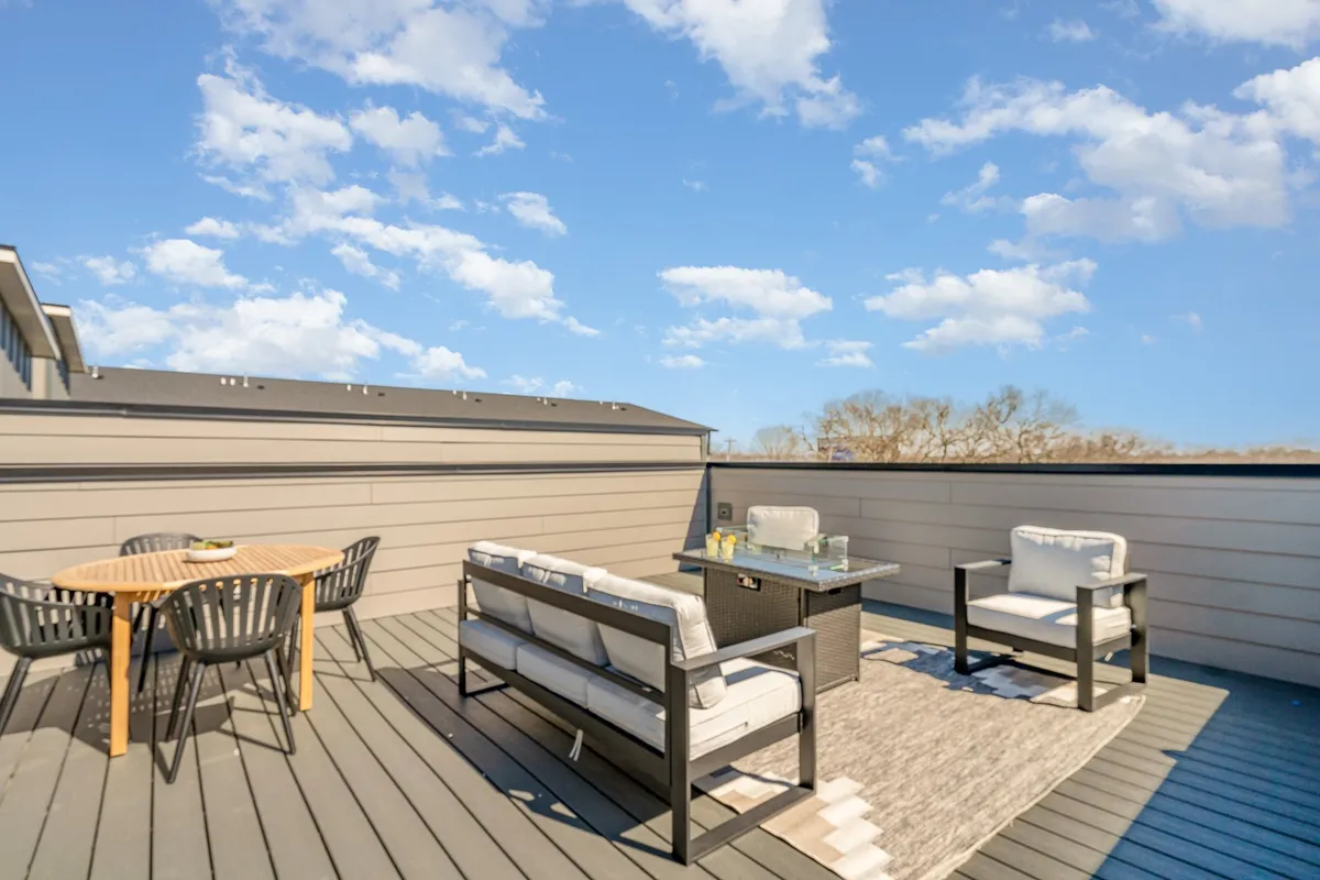 A chic third-floor balcony setup with comfortable lounge seating, a dining table ready for al fresco meals, a decorative rug, and lush potted plants, all bathed in natural light. The balcony feels private yet open, ideal for morning coffee or an intimate meal as a group.
