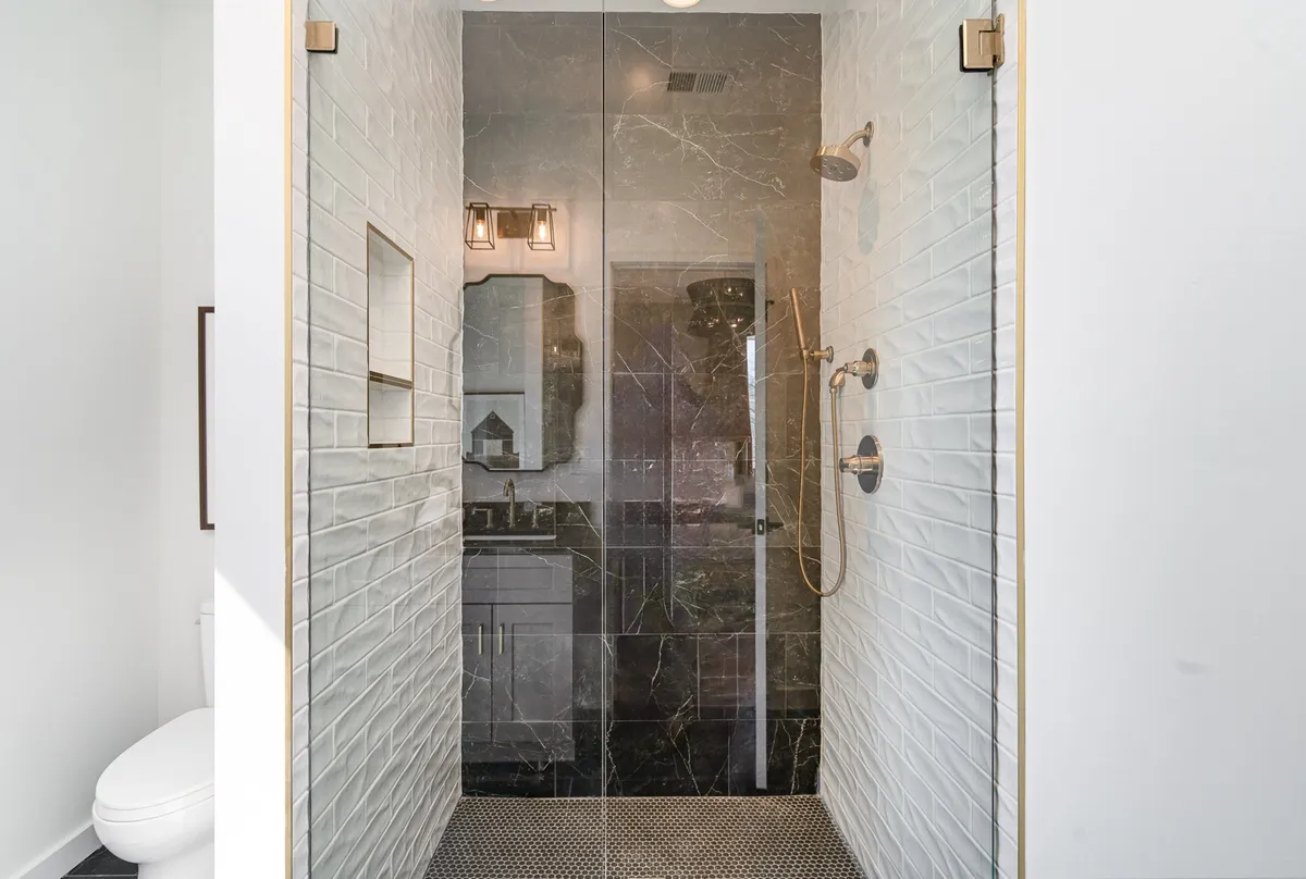 A modern bathroom with a walk-in shower, black marble tiles, textured white walls, and sleek lighting. The space feels luxurious and serene, conveying cleanliness and thoughtful design.