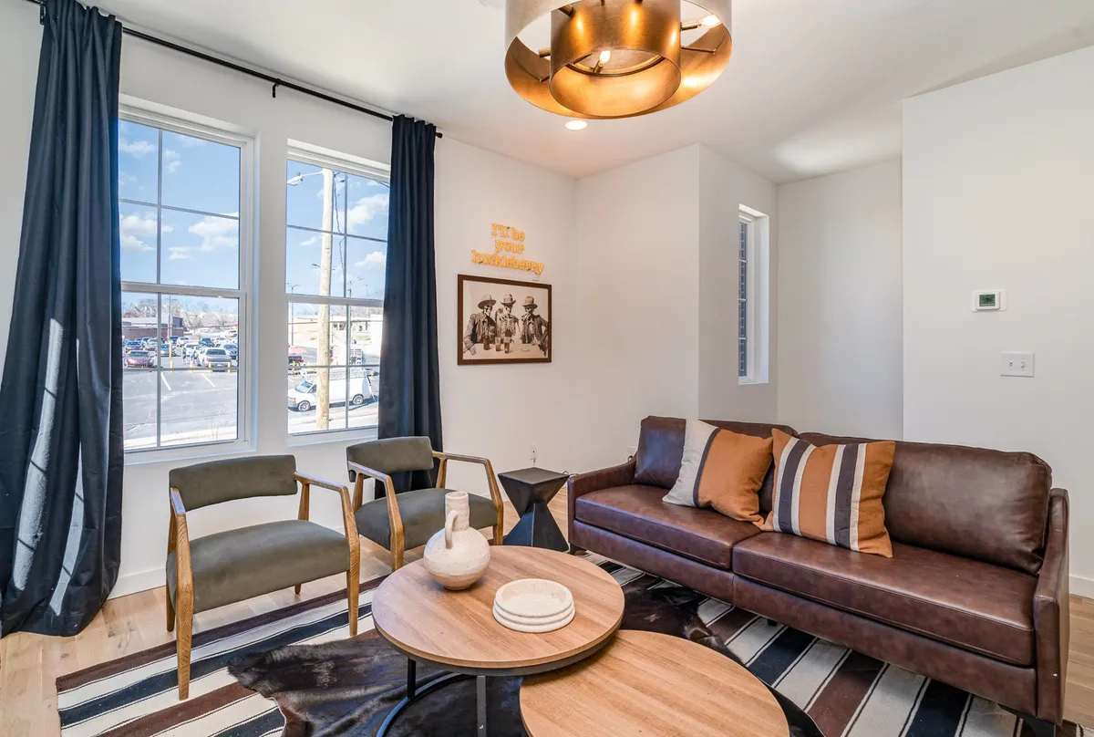 A comfortable living room with a plush sofa, a modern coffee table, decorative artwork, and large windows letting in natural light. The mood is cozy and inviting, ideal for socializing or unwinding with family and friends.