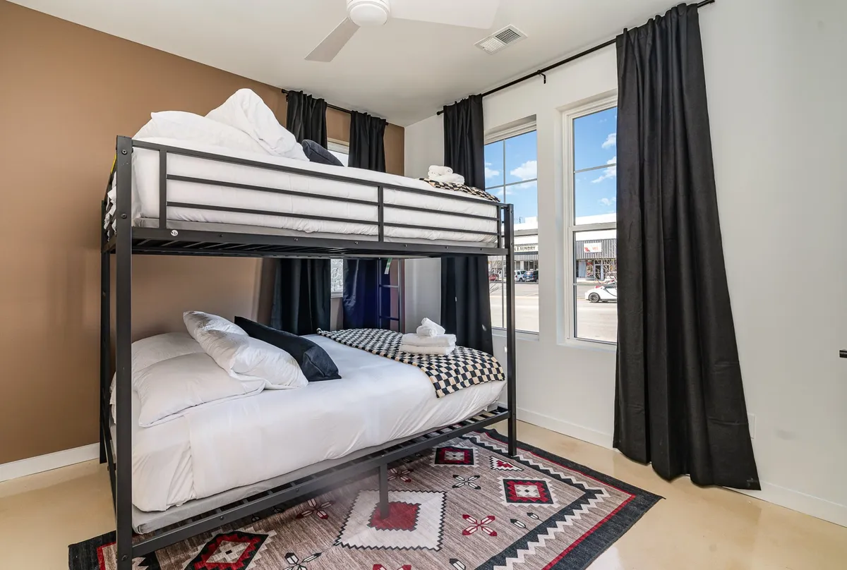 This image captures a playful and inviting bunk-style bedroom, featuring a bunk bed, soft rug, and windows letting in natural light. The space feels perfect for relaxation or sharing fun moments, suited for families or groups of friends.