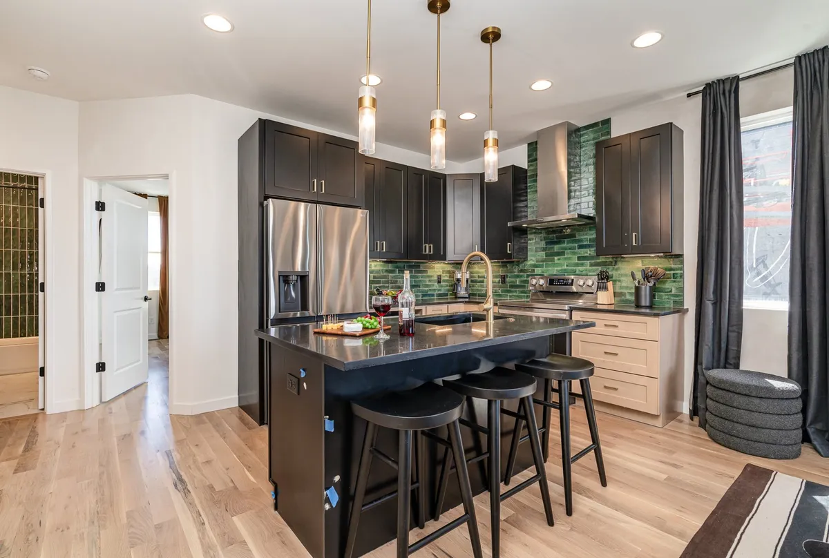 A contemporary kitchen scene featuring a large island countertop, sleek stainless steel appliances, a fresh green backsplash, and comfortable seating. The setting exudes modern warmth, ideal for prepping breakfast or sharing evening cocktails.