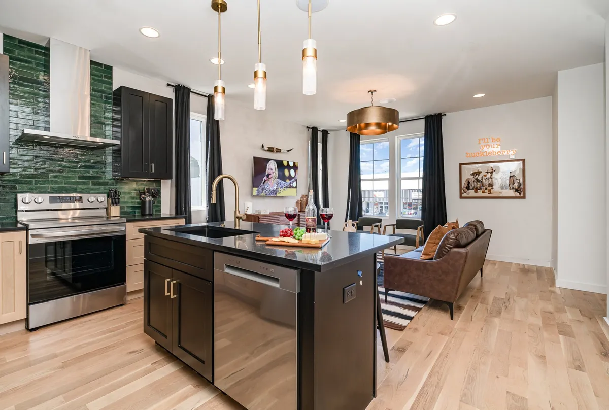 A wide view of the open-concept kitchen and dining area, featuring a spacious kitchen island, dark cabinetry, a green backsplash, a dining area, and vibrant Southwestern-inspired artwork. The space is well-lit and designed to encourage group gatherings for cooking, dining, and conversation.