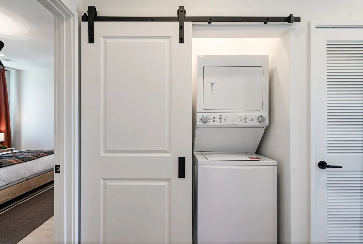 A bright, organized laundry room featuring a washing machine and dryer behind a sliding barn door. The space is clean, practical, and inviting, emphasizing ease and efficiency for everyday living.