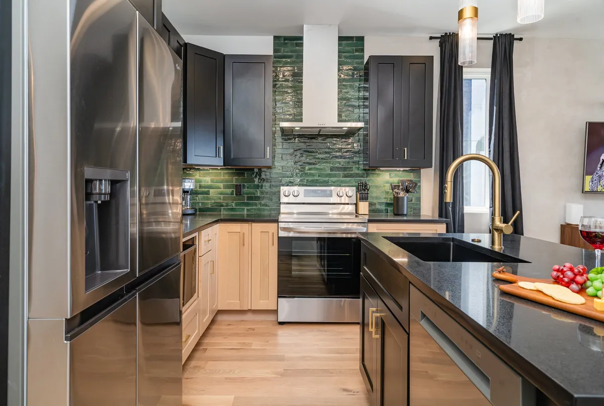 A stylish kitchen showcasing black cabinets, a green backsplash, stainless steel appliances, and a roomy kitchen island—perfect for preparing meals or social gatherings.