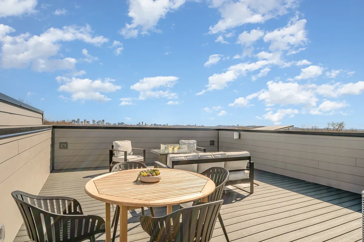 A beautifully staged rooftop dining and seating area with a dining table set for a meal, plush seating, and the city skyline stretching out in the distance. The atmosphere is relaxed, social, and perfect for evening gatherings or brunch with friends while watching the city lights.